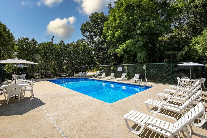 Inviting outdoor pool area with comfortable lounge chairs, surrounded by lush greenery and blue sky, perfect for relaxation.