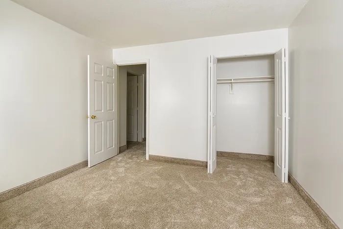 Bright, spacious bedroom with plush carpet, featuring an open closet and two doors for convenient access.