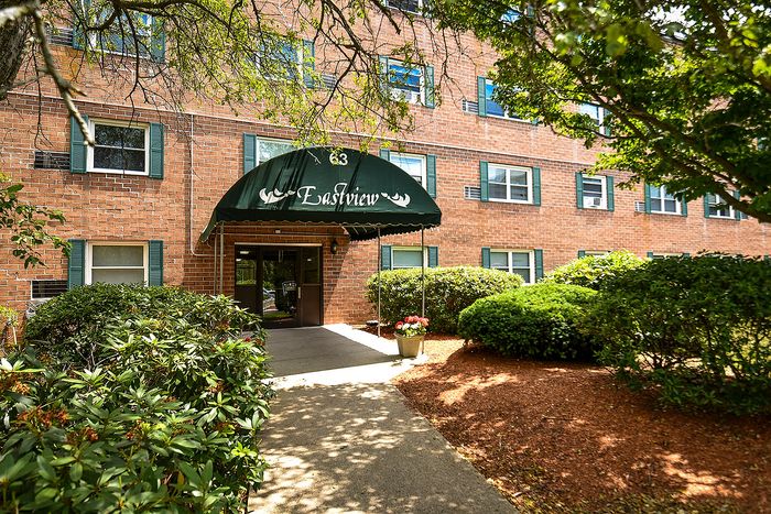 Charming apartment building entrance with lush greenery, Eastview awning, and inviting walkway.