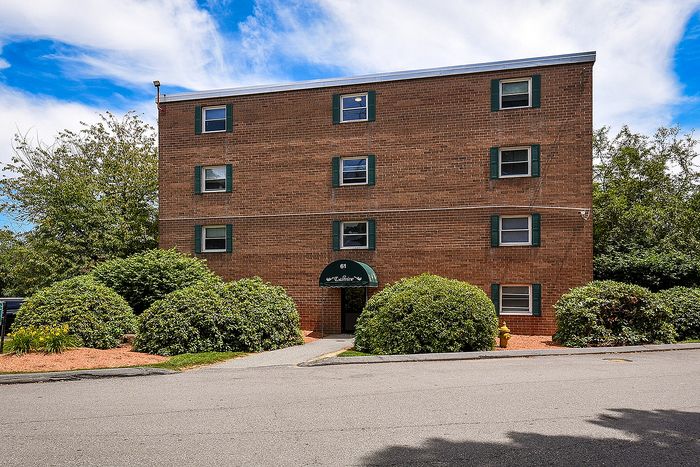 Charming brick apartment building with elegant arched entrance, framed by lush greenery and vibrant blue skies.