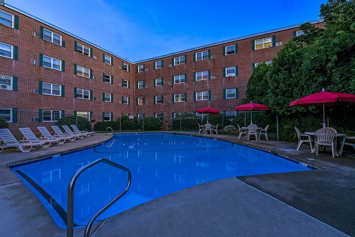 Inviting apartment complex courtyard featuring a sparkling blue swimming pool, surrounded by comfortable lounge chairs and vibrant red umbrellas for a relaxing atmosphere.