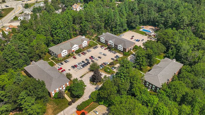 Charming aerial view of a tranquil apartment complex surrounded by lush greenery, featuring ample parking and spacious buildings, perfect for serene suburban living.