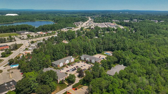 Charming aerial view of a tranquil neighborhood nestled amidst lush greenery, featuring quaint apartment buildings and scenic surroundings.