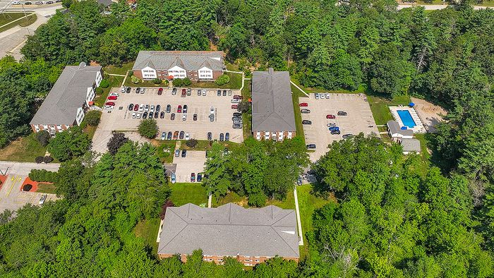 Aerial view of a tranquil apartment complex surrounded by lush greenery, featuring ample parking and a refreshing swimming pool.