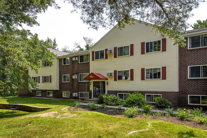 Inviting residential building with charming brick and siding facade, surrounded by lush greenery and a manicured front lawn.