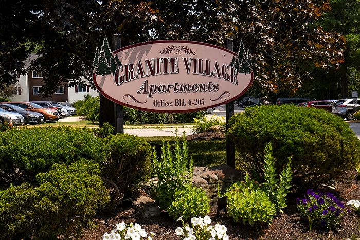 Charming Granite Village Apartments sign surrounded by lush greenery and vibrant flowers, highlighting a welcoming atmosphere.