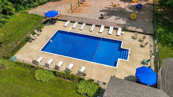 Inviting aerial view of a sparkling blue swimming pool surrounded by sun loungers, vibrant umbrellas, and lush greenery, complete with a nearby playground for family enjoyment.