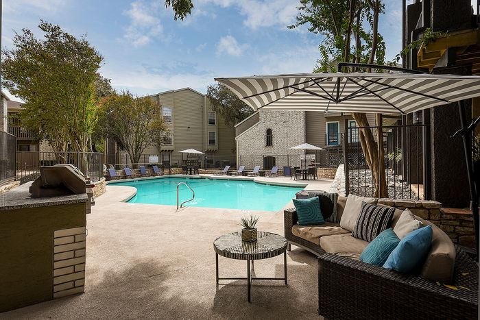 Inviting apartment courtyard featuring a sparkling pool, stylish lounge chairs, and cozy seating under a striped canopy, perfect for relaxation.