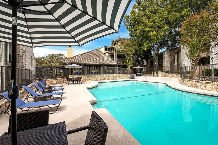 Inviting apartment courtyard featuring a pristine swimming pool with stylish loungers, shaded seating, and lush greenery.