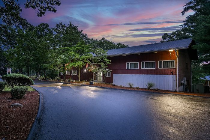 Charming evening view of a modern rustic building surrounded by lush greenery, enhanced by a vibrant sunset sky.