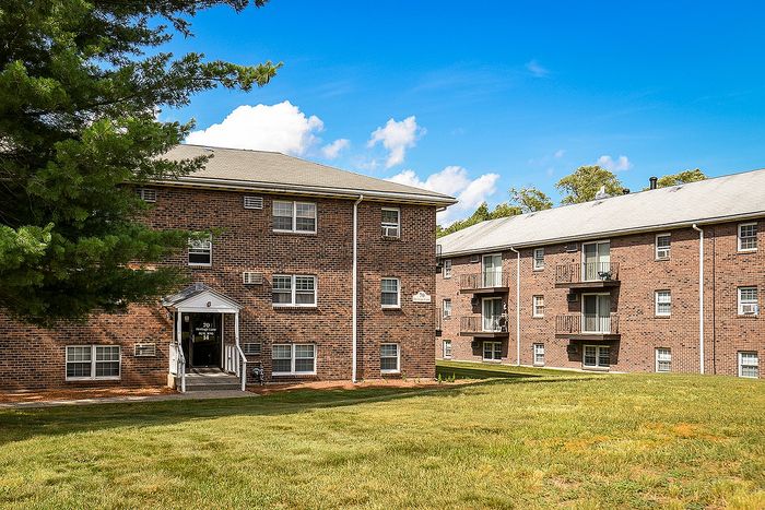 Charming brick apartment complex surrounded by lush greenery and bright blue skies, perfect for tranquil living.