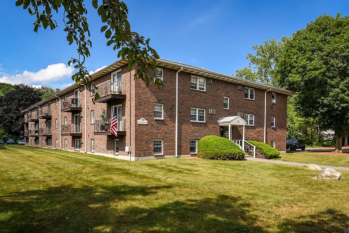 Charming brick apartment complex with lush green lawn and inviting balconies, set under a clear blue sky.