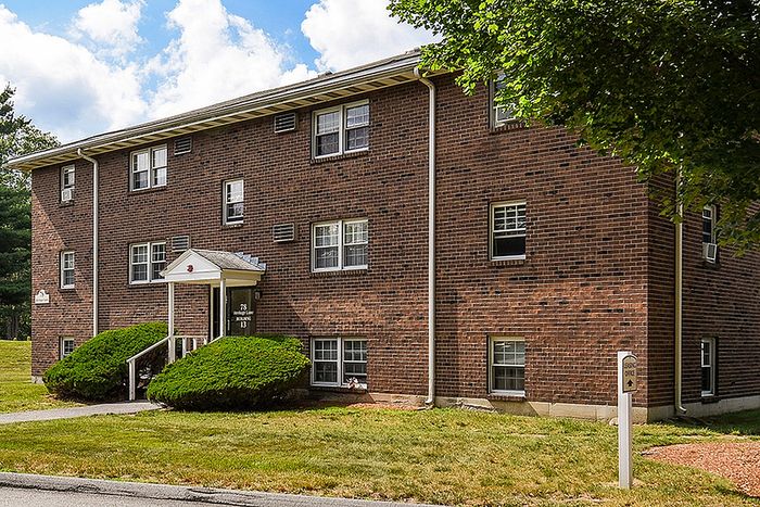 Charming brick apartment building with lush green landscaping and a welcoming entrance, ideal for a serene living experience.