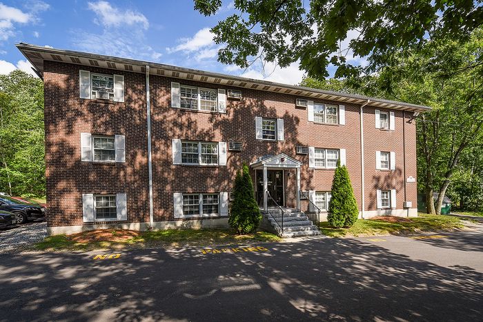 Charming brick apartment building with white-trimmed windows, nestled in a serene setting surrounded by lush greenery.