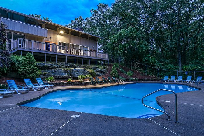 Serene apartment pool area surrounded by lush greenery and inviting lounge chairs under a twilight sky.