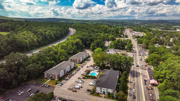 Aerial view of a picturesque suburban area with residential buildings, lush greenery, and a sparkling swimming pool, showcasing the charm and accessibility of the neighborhood.