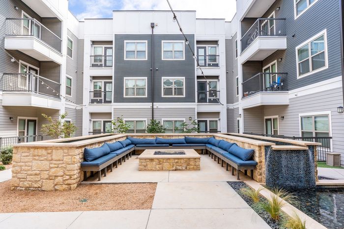 Modern apartment courtyard with elegant water feature, stone seating area, and inviting blue cushioned benches.
