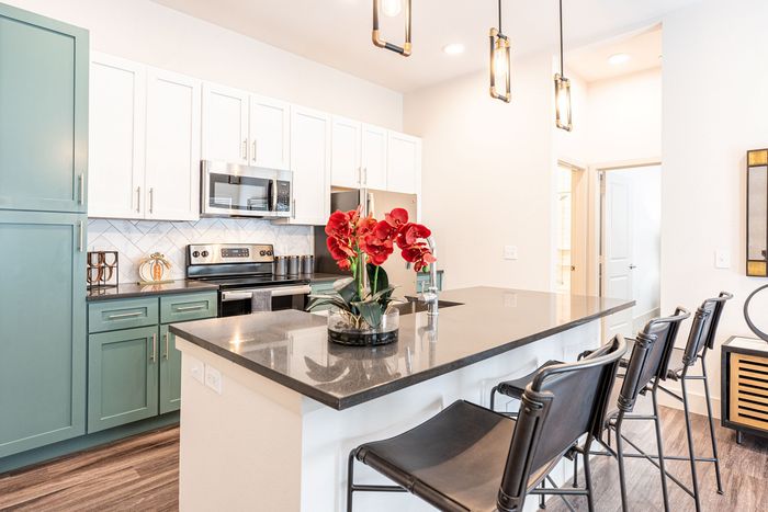 Chic modern kitchen with elegant granite countertops, stylish pendant lighting, and vibrant red floral decor. Features sleek stainless steel appliances and inviting seating at the island bar.
