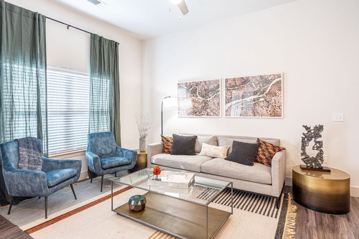 Contemporary living room with elegant decor, featuring a plush gray sofa, stylish blue armchairs, chic glass coffee table, and modern art pieces.