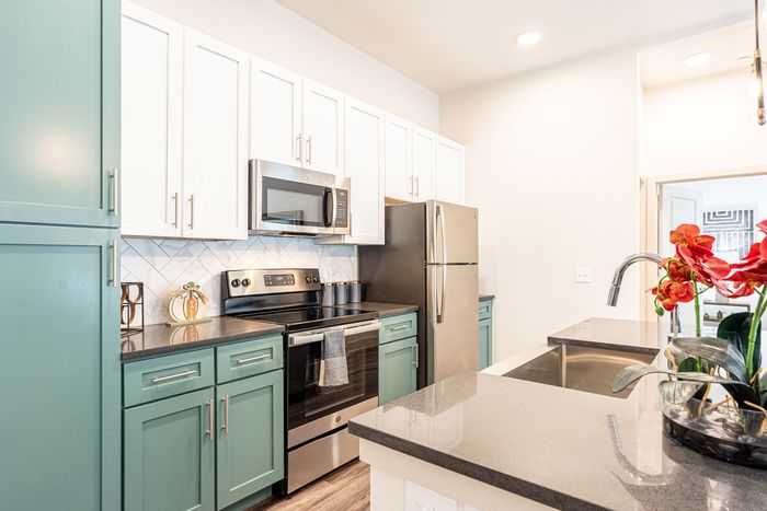 Contemporary kitchen with sleek stainless steel appliances, vibrant teal and white cabinetry, and chic granite countertops, accentuated by fresh red flowers.