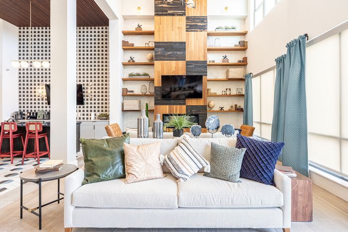 Chic and modern living room with stylish decor, featuring a plush sofa with colorful cushions, elegant shelving, and a large TV, bathed in natural light from expansive windows.