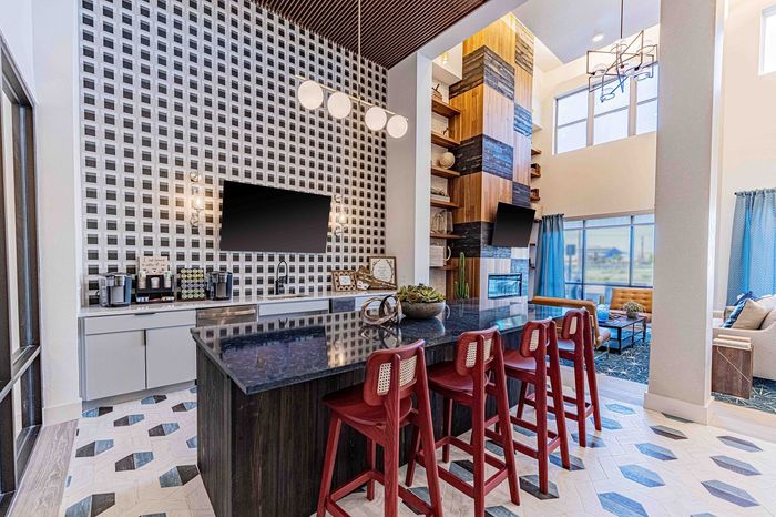 Chic apartment interior with a modern kitchen bar, red stools, stylish geometric backsplash, and open-concept living area with large windows.