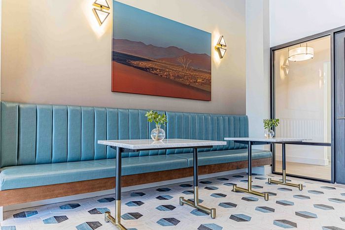 Chic apartment dining area with modern art, sleek blue booth seating, and elegant geometric floor tiles.