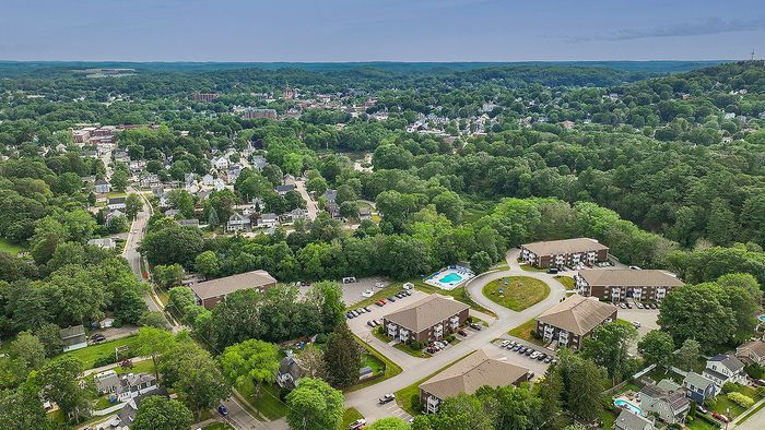 Charming aerial view of a vibrant neighborhood surrounded by lush greenery, featuring modern apartment complexes and a refreshing community pool.