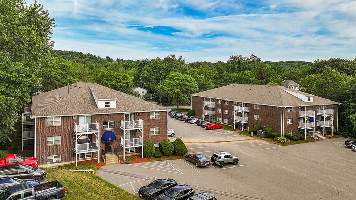 Charming brick apartment complex surrounded by lush greenery, featuring private balconies and ample parking space in a tranquil setting.