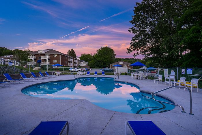Charming apartment community with a serene poolside view, lounge chairs, and stunning sunset skies.