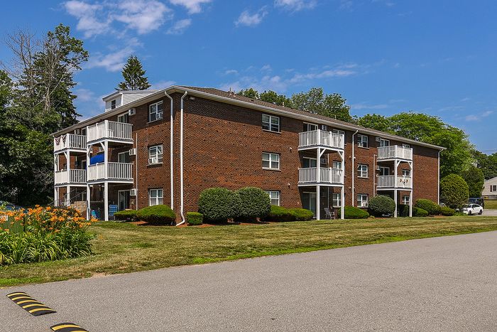 Charming red brick apartment building with inviting balconies and lush landscaping under a bright blue sky.