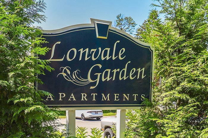 Charming Lonvale Garden Apartments sign surrounded by lush greenery under a clear blue sky.