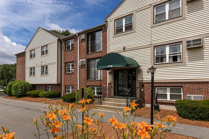 Charming apartment building with brick facade and green awning, surrounded by vibrant orange flowers and lush greenery.