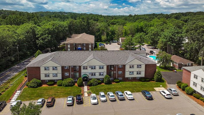 Charming apartment complex surrounded by lush greenery, featuring ample parking and a refreshing swimming pool for residents.