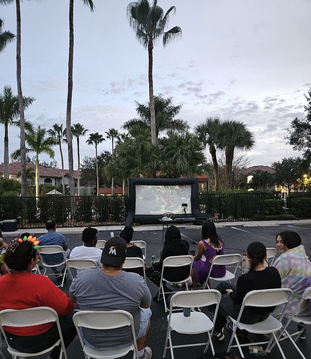Charming outdoor movie night in a lush garden setting, with comfortable seating and towering palm trees under the evening sky.