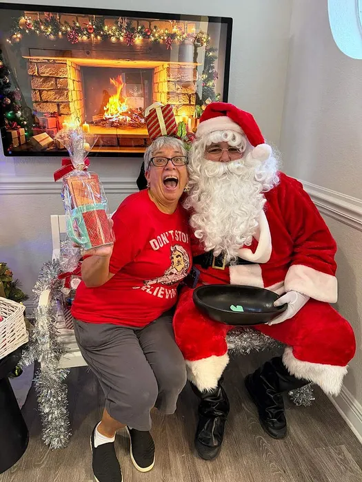 Joyful holiday scene with Santa Claus and an excited person holding a gift, set against a cozy fireplace backdrop.