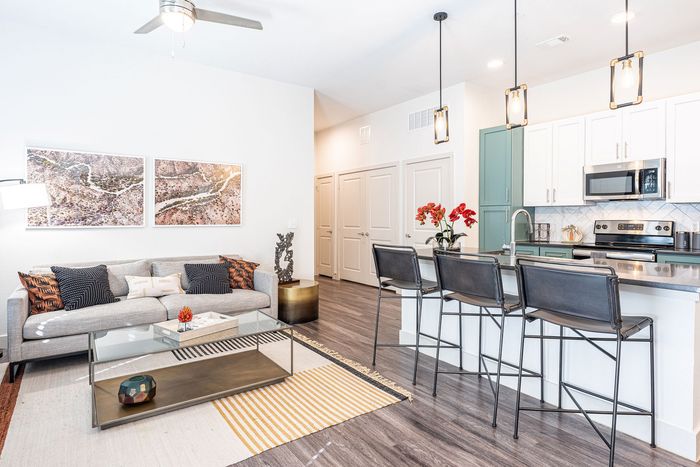 Modern apartment with a stylish open-concept living area, featuring a cozy gray sofa, vibrant art pieces, and a sleek kitchen with a chic breakfast bar and pendant lighting.