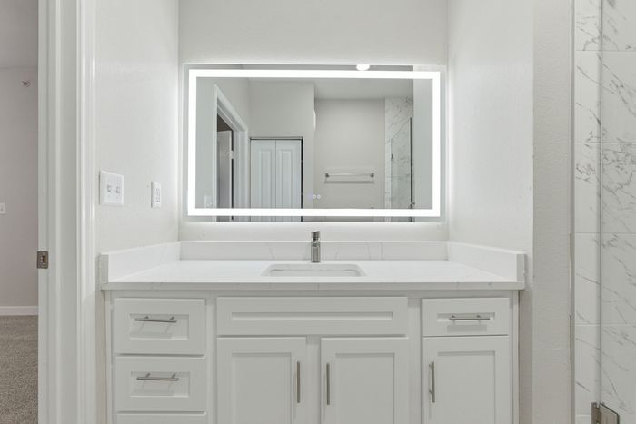 Modern bathroom with illuminated mirror and sleek white cabinetry, exuding elegance and contemporary style.
