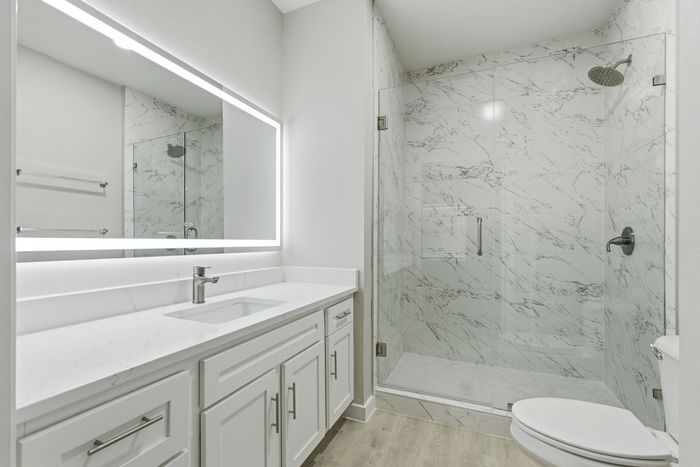 Elegant bathroom featuring a sleek vanity with marble countertop, illuminated mirror, and a spacious glass-enclosed shower with modern tile design.