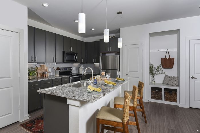 Contemporary kitchen with sleek dark cabinetry, granite countertops, and ambient pendant lighting. Features a stylish breakfast bar with chic wicker chairs, perfect for modern living.