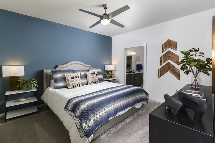 Elegant bedroom with a plush bed featuring blue and white accents, stylish wall art, and modern ceiling fan, creating a serene and inviting retreat.