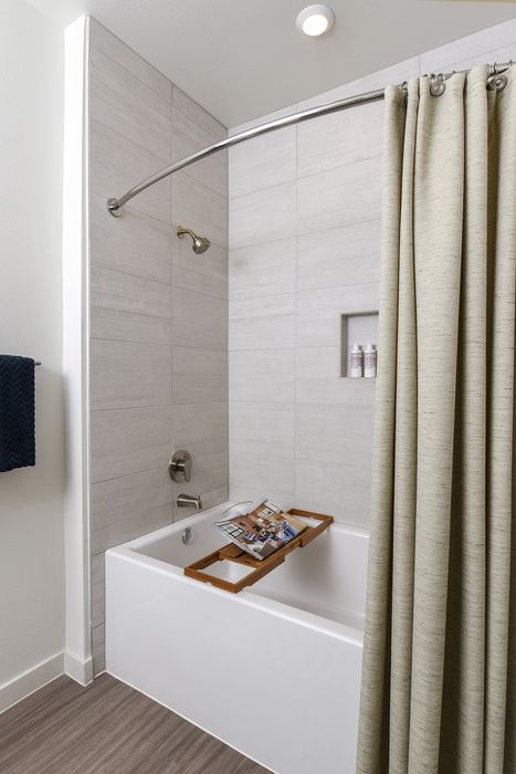 Modern bathroom with elegant tile walls, a sleek bathtub featuring a wooden tray, and stylish accessories for a luxurious feel.