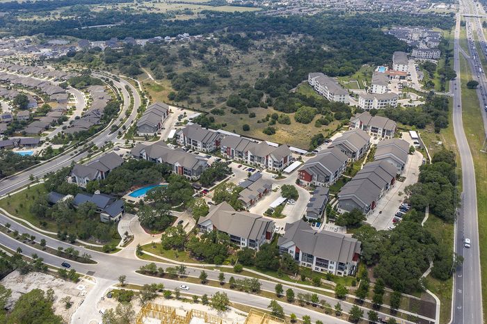 Aerial view of a modern apartment community featuring elegant architecture, lush landscaping, and inviting swimming pools, surrounded by scenic green spaces and winding roads.