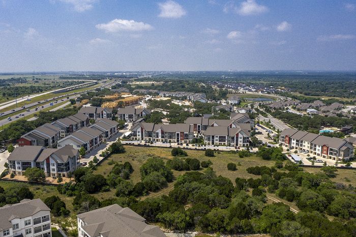 Expansive aerial view of a vibrant apartment community surrounded by lush greenery and modern amenities, offering a serene and convenient lifestyle.