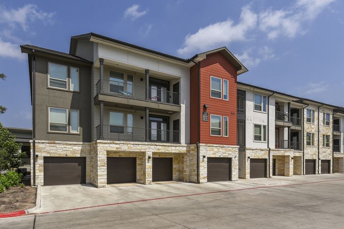 Modern apartment complex with elegant stone facade, private balconies, and attached garages under a clear blue sky.