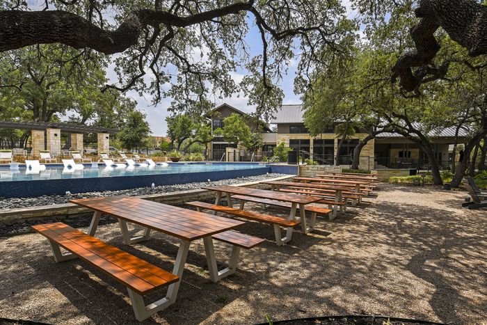 Inviting outdoor space with picnic tables, a stunning pool with lounge chairs, nestled under the shade of majestic trees.