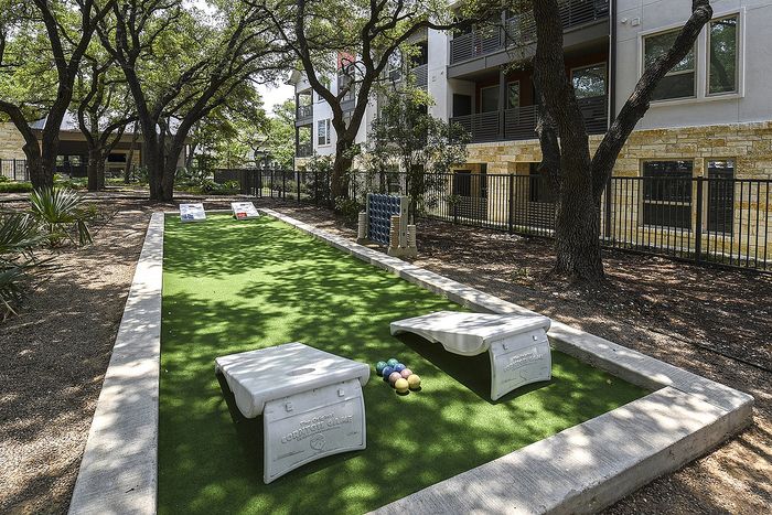 Inviting outdoor recreation area featuring a cornhole game set on a lush green space, surrounded by mature trees and a stylish apartment building.