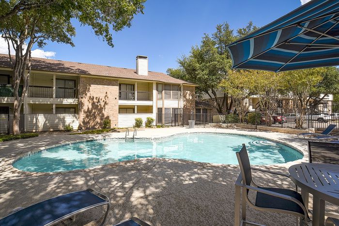 Charming apartment complex with inviting swimming pool, shaded seating, and lush greenery.