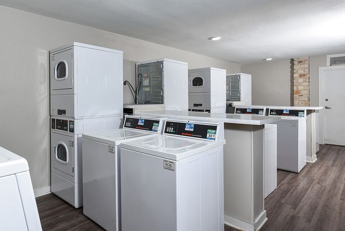 Modern laundry room with multiple washers and dryers, bright lighting, and sleek countertops for a convenient living experience.
