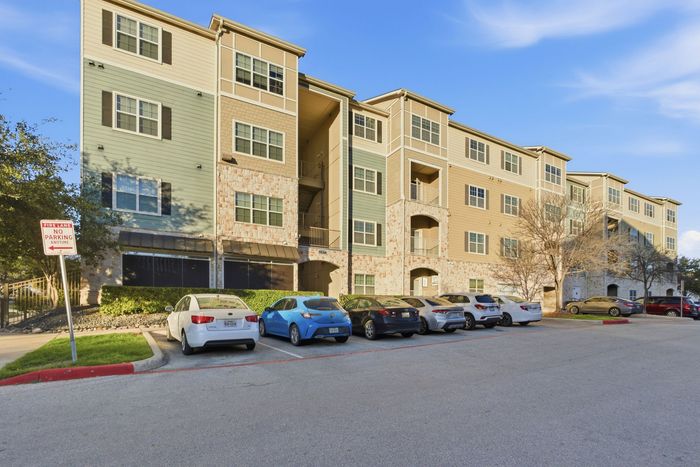 Charming four-story apartment complex with a modern design, featuring stone accents and large windows, set against a clear blue sky. Convenient parking available in front.